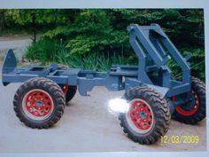 an old blue truck with red wheels parked in front of some bushes and trees on the other side