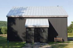 a black building with a metal roof and wooden bench in front of it on the grass