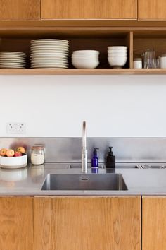 a stainless steel sink in a kitchen with wooden cabinets and dishes on the shelf above it