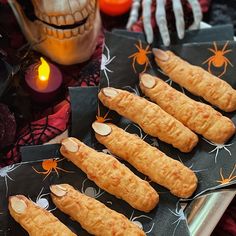 halloween treats are arranged on black paper and decorated with spider webs, pumpkins and candles