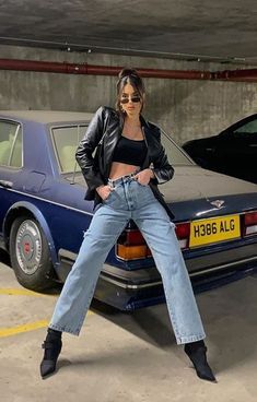 a woman leaning on the back of a car in a parking garage with her legs crossed