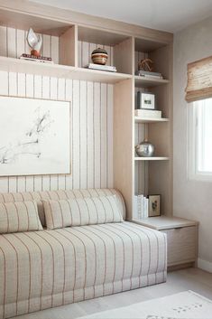 a white couch sitting under a window next to a shelf filled with vases and books