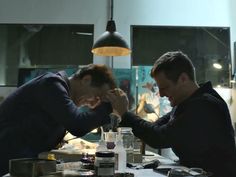 two men sitting at a table in front of a mirror with their hands on each other's head