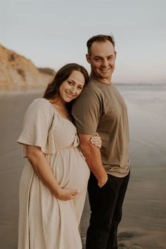 a pregnant couple standing next to each other on the beach