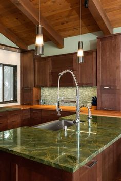 a kitchen with green marble counter tops and wooden cabinets, along with two pendant lights hanging from the ceiling