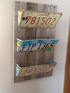 three license plates mounted to the side of a wooden wall hanging on a white wall