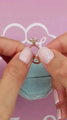 a woman's hands holding an engagement ring in front of a pink box with the word love written on it