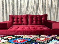 a red couch sitting on top of a rug in front of a curtained wall