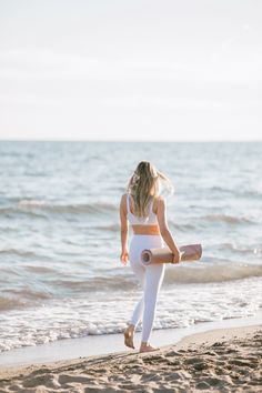 a woman is walking on the beach with a yoga mat