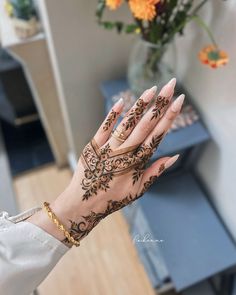 a woman's hand with henna tattoos on it and flowers in the background