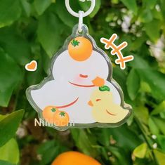 a keychain with an orange on it is hanging from a tree in front of some leaves