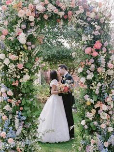 a bride and groom kissing in front of a floral arch