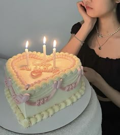 a woman sitting in front of a heart shaped cake with lit candles on the top