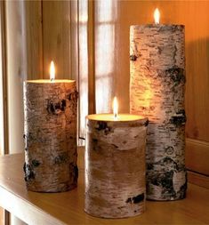 three lit candles sitting on top of a wooden shelf in front of a window sill