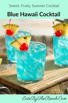 two glasses filled with blue liquid and topped with a pineapple, cherries, and a cherry