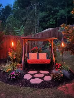 a swing bed in the middle of a garden at night with candles lit up around it