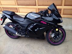 a black motorcycle parked in front of a garage door with pink rims on it