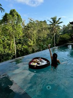 a woman is in the water with her hand up and some food on a tray