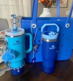 a blue tote bag, two mugs and a necklace on a wooden table