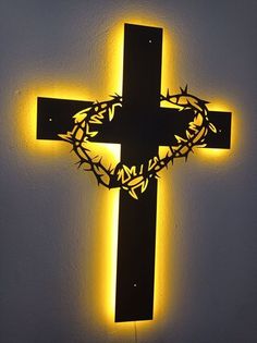 a lighted cross with a crown of thorns on the top is lit up against a white wall