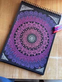 a spiral notebook with an intricate design on the cover and colored pencils next to it