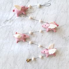 three pink and white elephant ornaments on a marble surface with bells in the shape of elephants