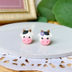 two small pink and white cow earrings sitting on top of a table