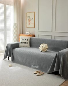 a living room with a gray couch covered in a blanket and slippers on the floor