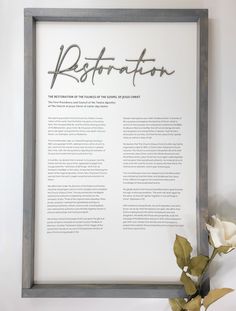 a framed sign with the words restoration written in cursive writing on it next to a white rose