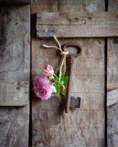 a pink flower is tied to an old rusty key on a wooden door with rope