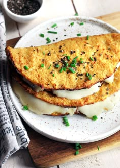 two pieces of food on a white plate with green onions and black pepper sprinkles