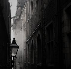 a street light in the middle of an alleyway with buildings on both sides and fog coming from behind it