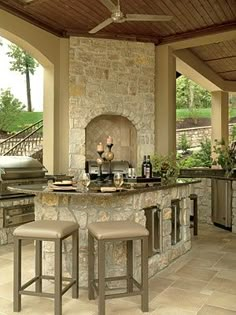 an outdoor kitchen with stone counter tops and bar stools, built into the ceiling