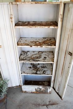 an old white cabinet with dirty paint on the bottom and shelves in front of it