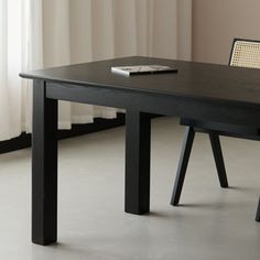 a black table with a book on it in front of a white curtained window