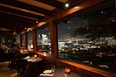 people sitting at tables in a restaurant overlooking the city lights