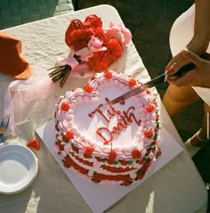 a birthday cake is being cut with a knife on a white tablecloth, surrounded by flowers and plates