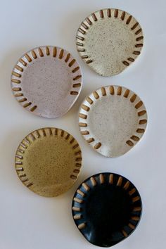 four small plates are arranged on a white surface, one is black and the other has brown speckles