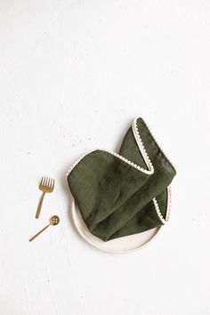 a green napkin and fork on a white plate next to a pair of silverware