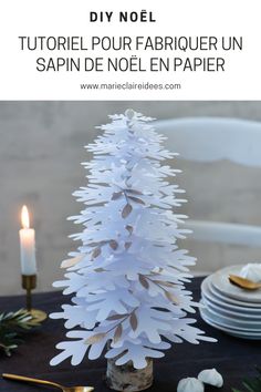 a small white christmas tree sitting on top of a table next to plates and candles