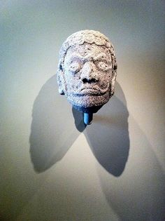 a stone head mounted on a wall with a shadow cast on the wall behind it