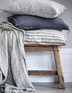 three pillows stacked on top of each other next to a wooden bench with a blanket draped over it