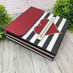 a red and black striped book with a heart on it sitting in front of some bushes