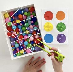 a child's hand is holding a plastic toy and next to a box filled with colored balls