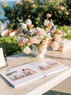 an open book sitting on top of a wooden table next to a vase filled with flowers