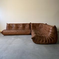 a brown leather couch sitting on top of a cement floor next to a white wall