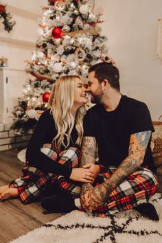 a man and woman are sitting in front of a christmas tree with their arms around each other