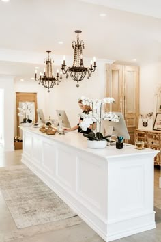 a woman sitting at a white counter in a room with chandeliers on the ceiling