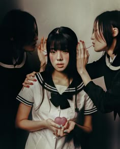 three young women standing next to each other in front of a wall holding an apple