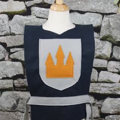 a blue and white apron with an orange crown on it's chest, next to a stone wall